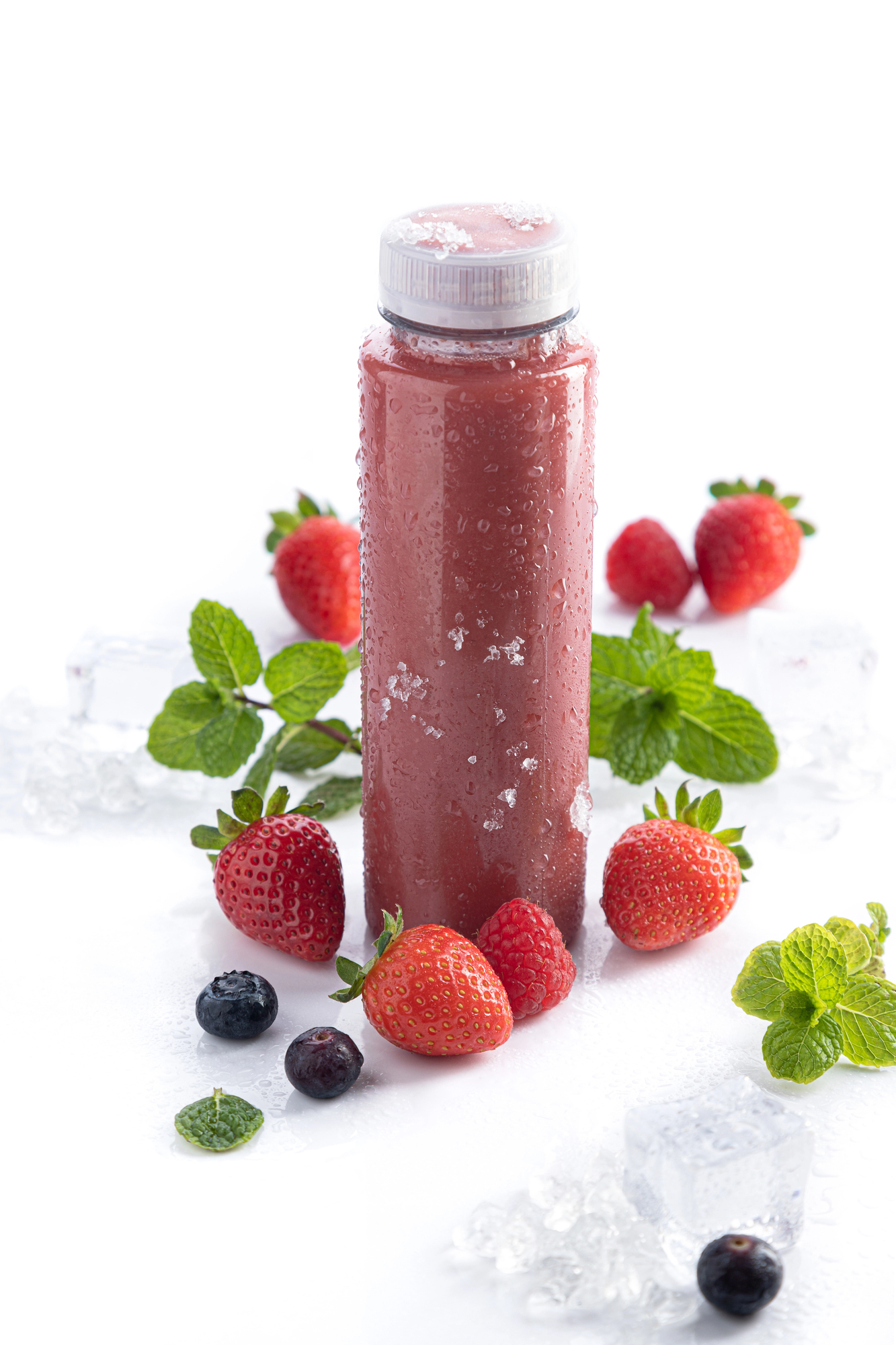 Bottle of red smoothie surrounded by fresh strawberries and berries