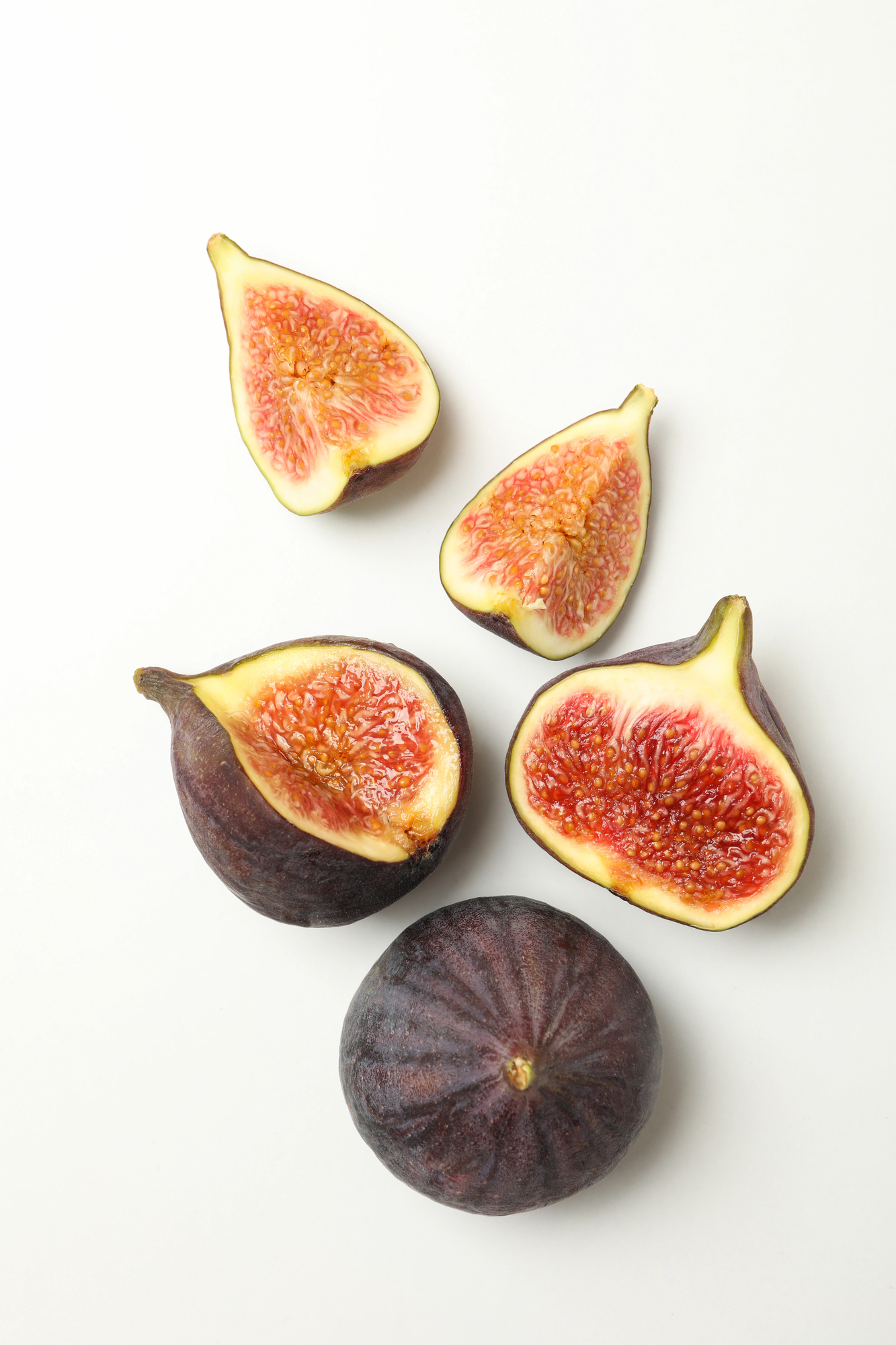 Four fig halves and one whole fig on white background