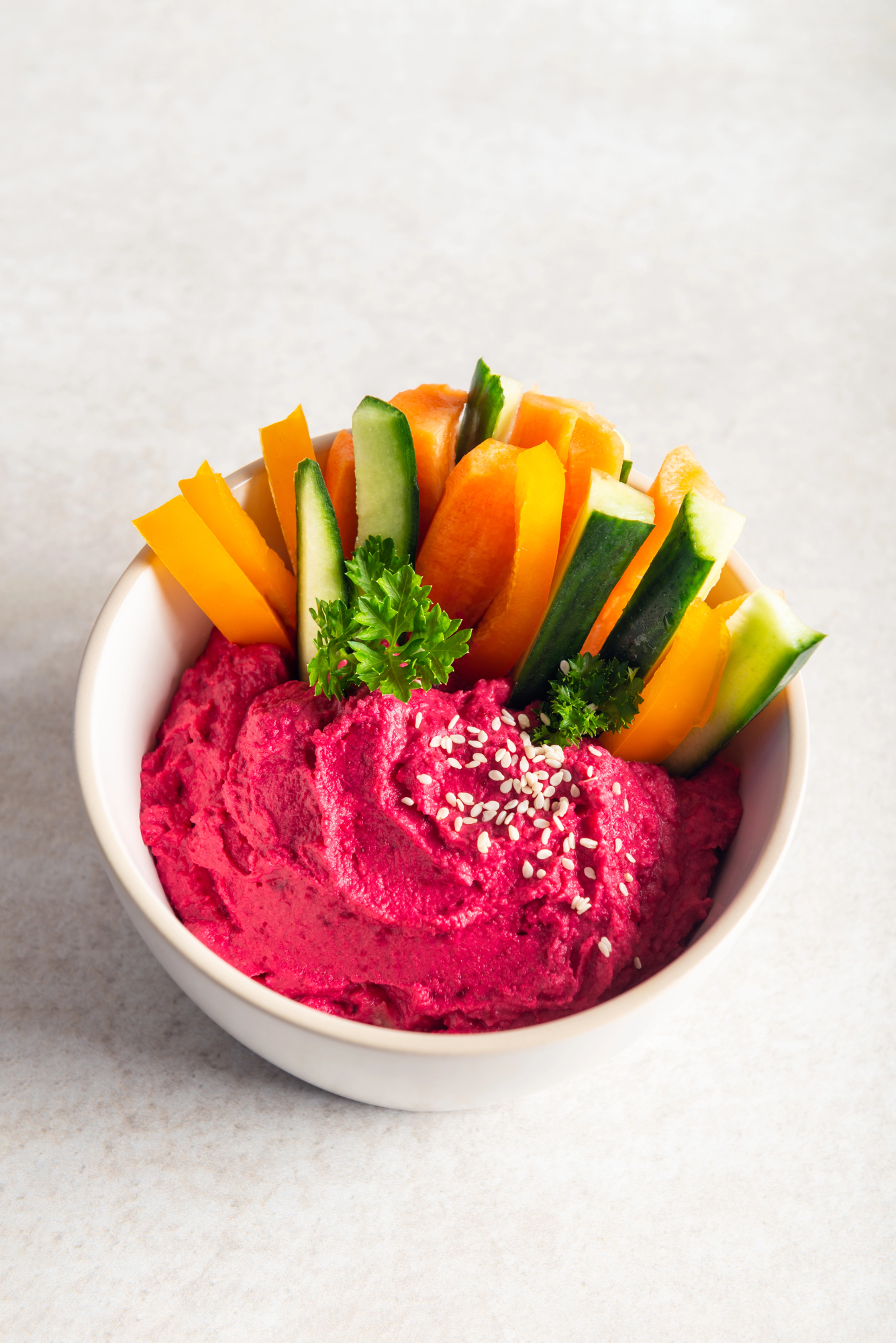 Beetroot hummus in white bowl with vegetable sticks