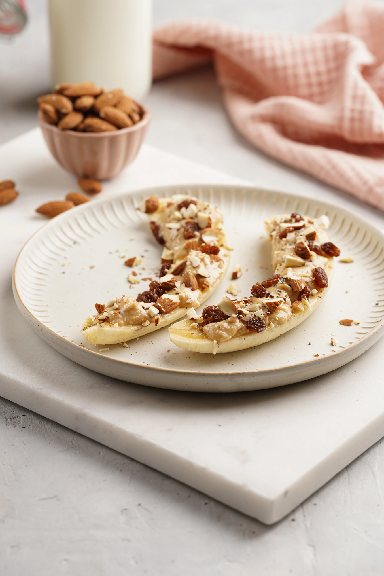 Banana halves with peanut butter and nuts on white plate