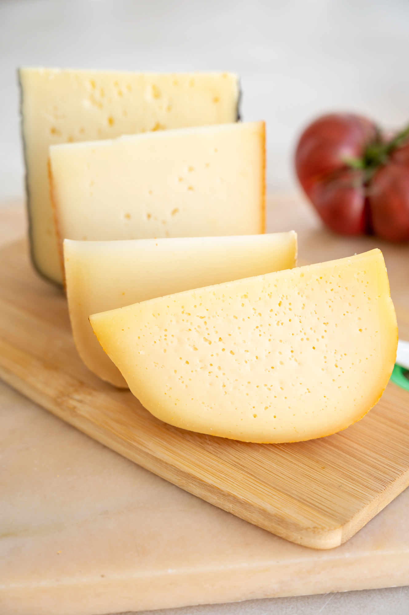 Four pale cheese wedges with small holes on a wooden board