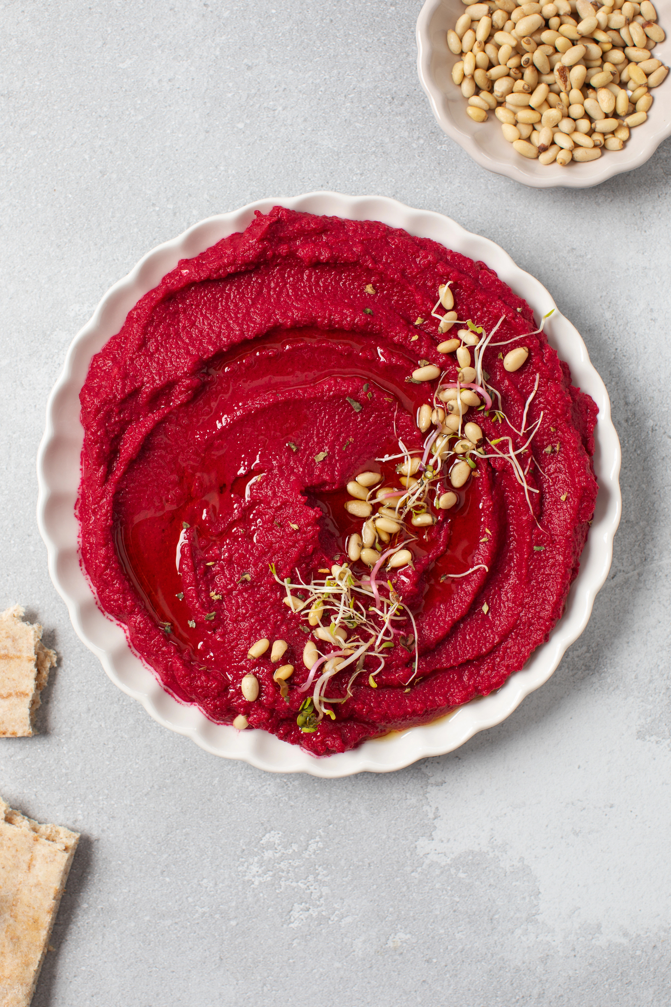 Beet hummus swirled in white bowl with pine nuts
