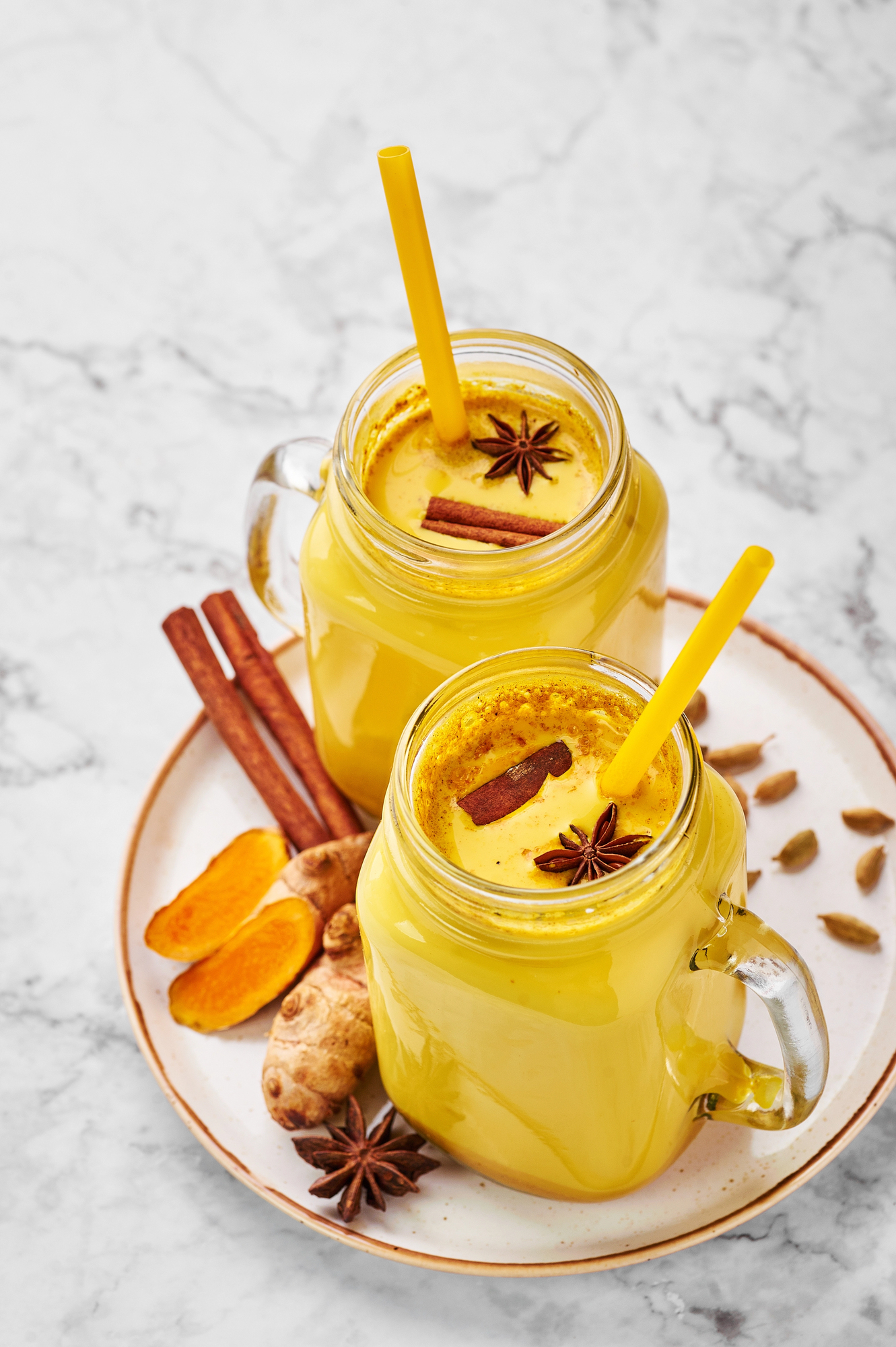 Two glasses of golden turmeric milk with star anise and cinnamon