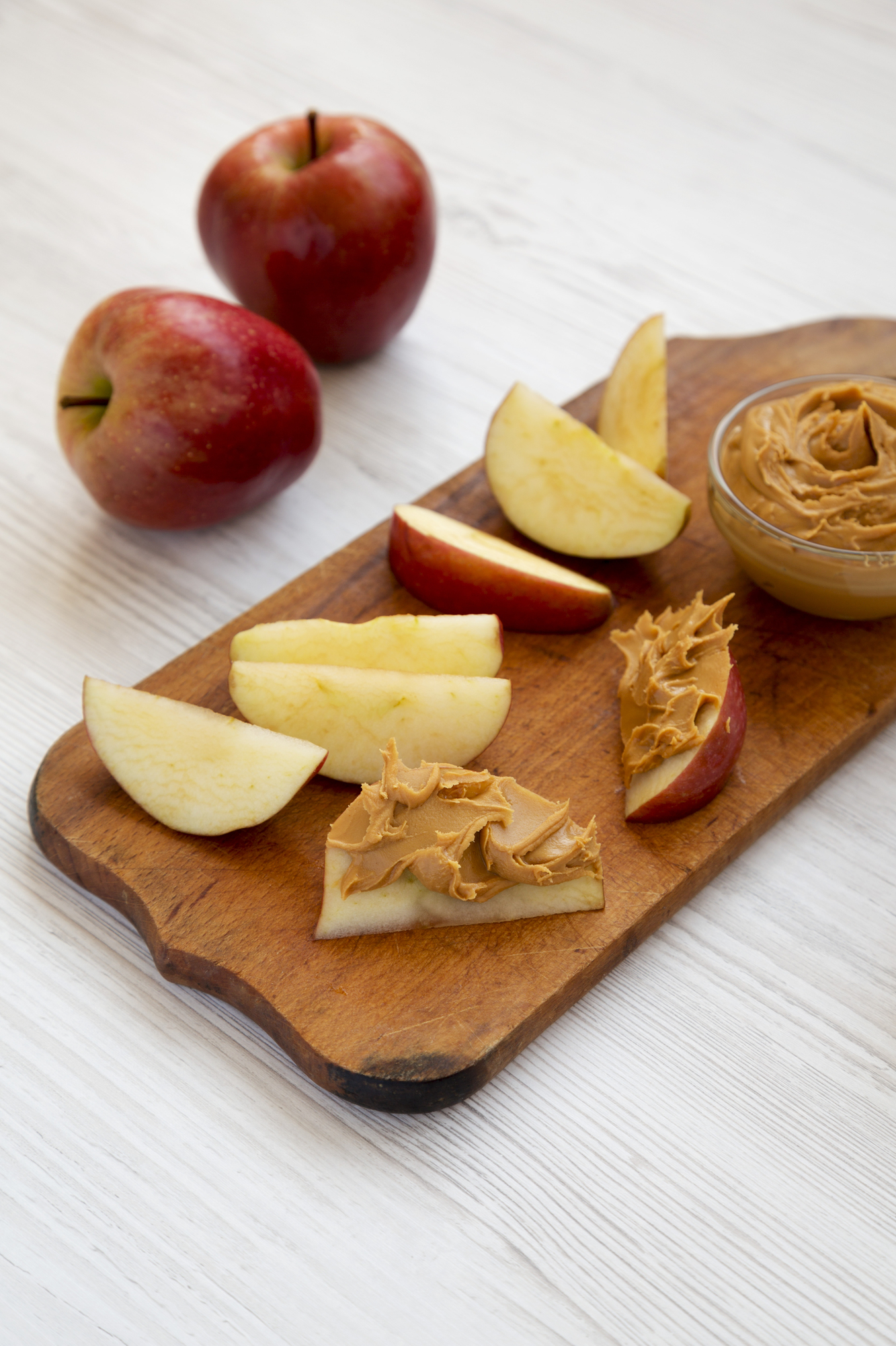 Red apples and sliced apples with peanut butter on wooden board