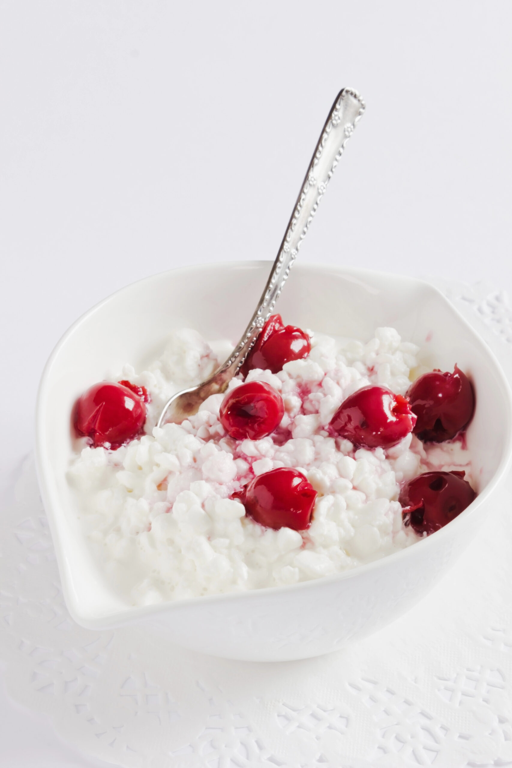 Bowl of cottage cheese with fresh red cherries and spoon