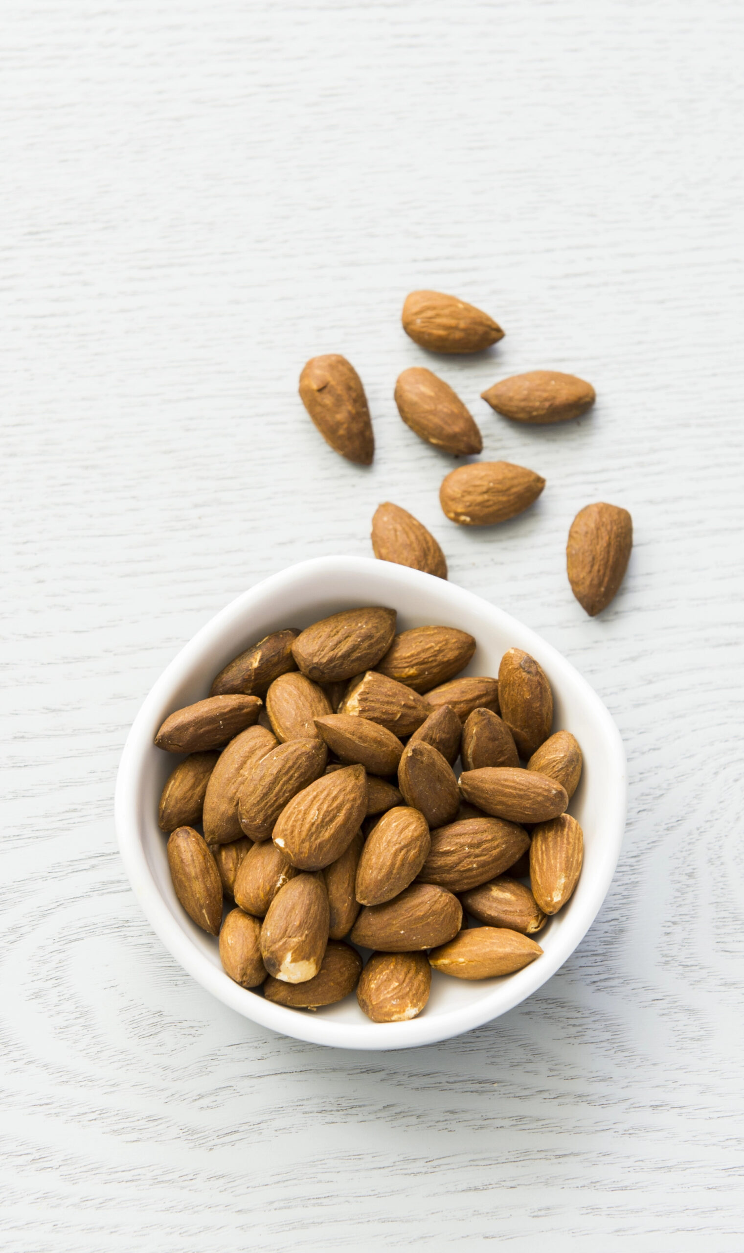 Bowl of shelled almonds with scattered almonds