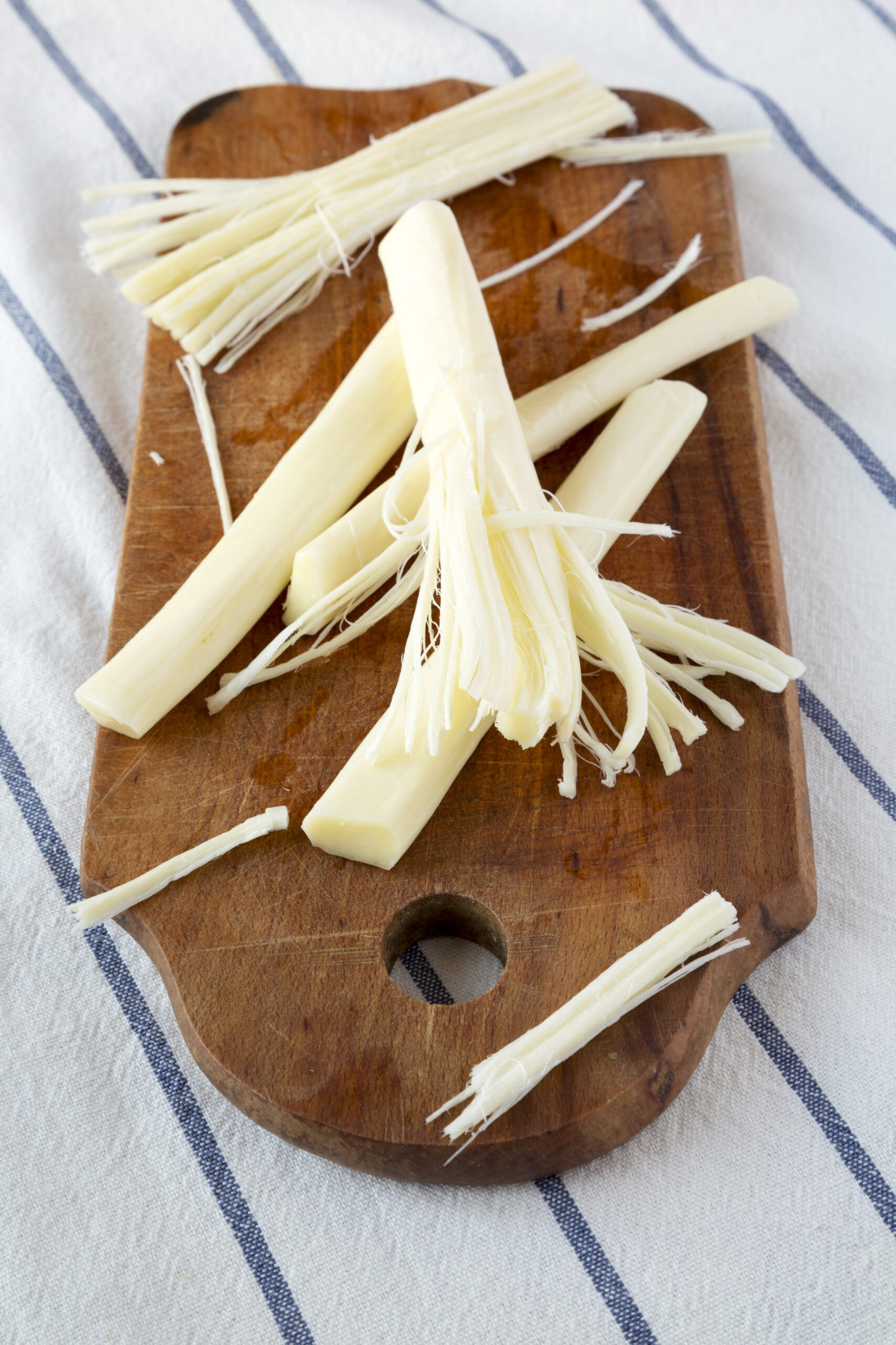 Peeled string cheese strips on wooden board