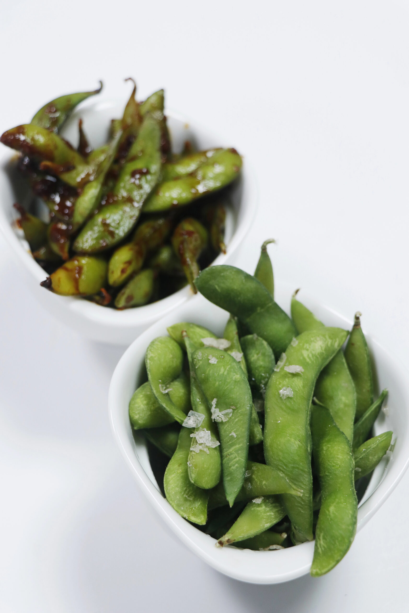 Steamed edamame pods in two white bowls
