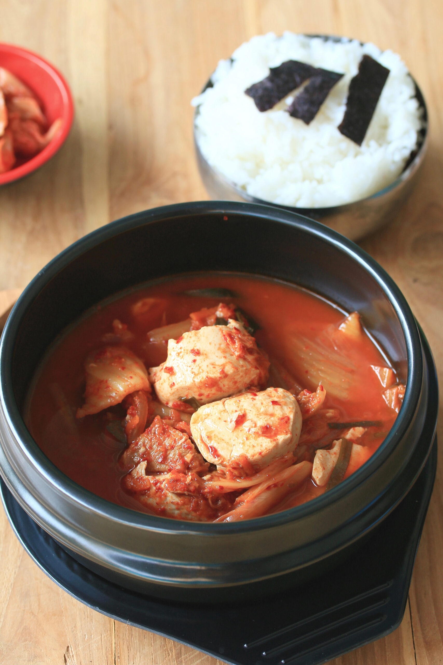 Kimchi soup with tofu and vegetables in black bowl