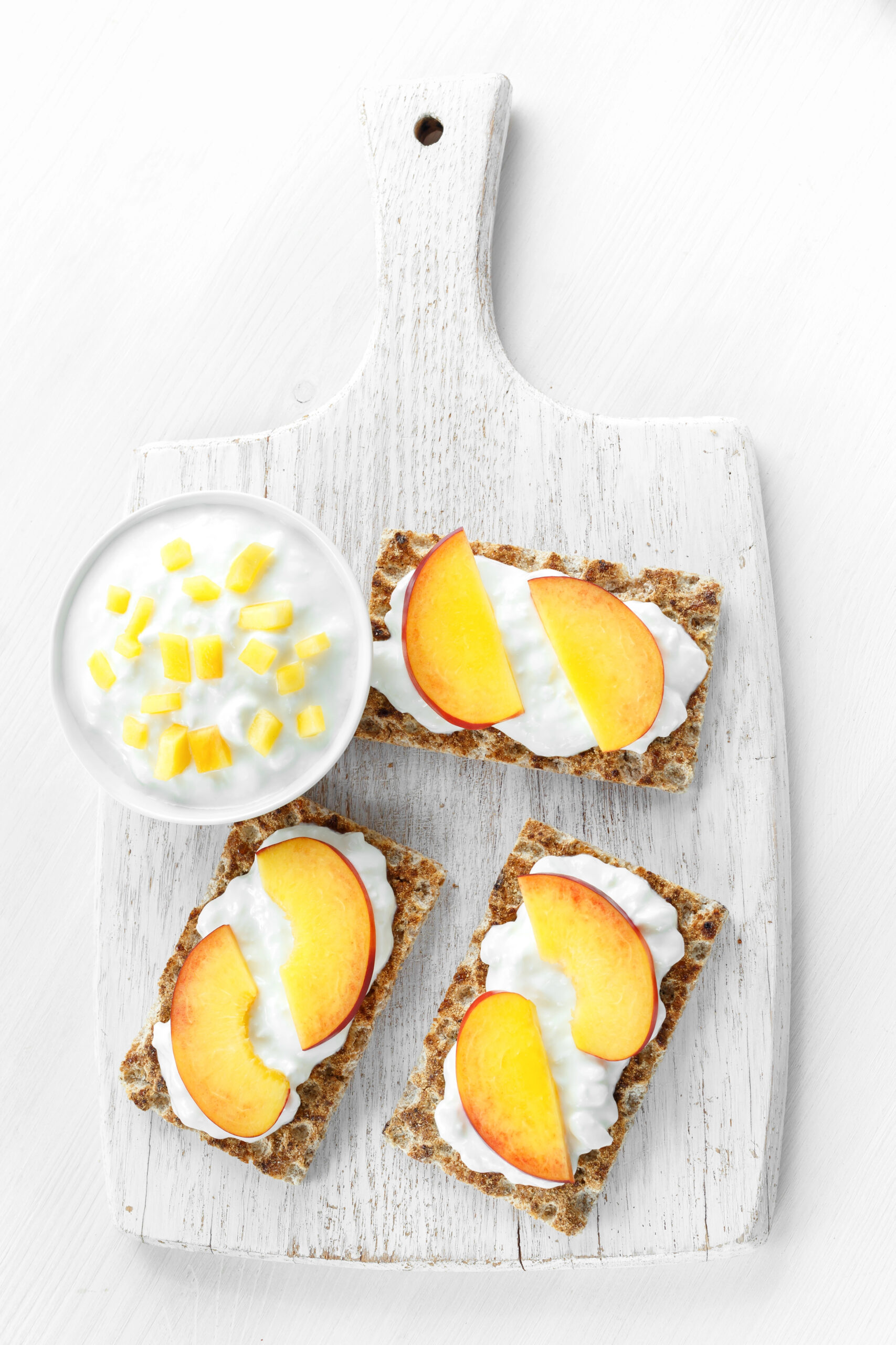 Three crispbread toasts with cottage cheese and nectarine slices on a board
