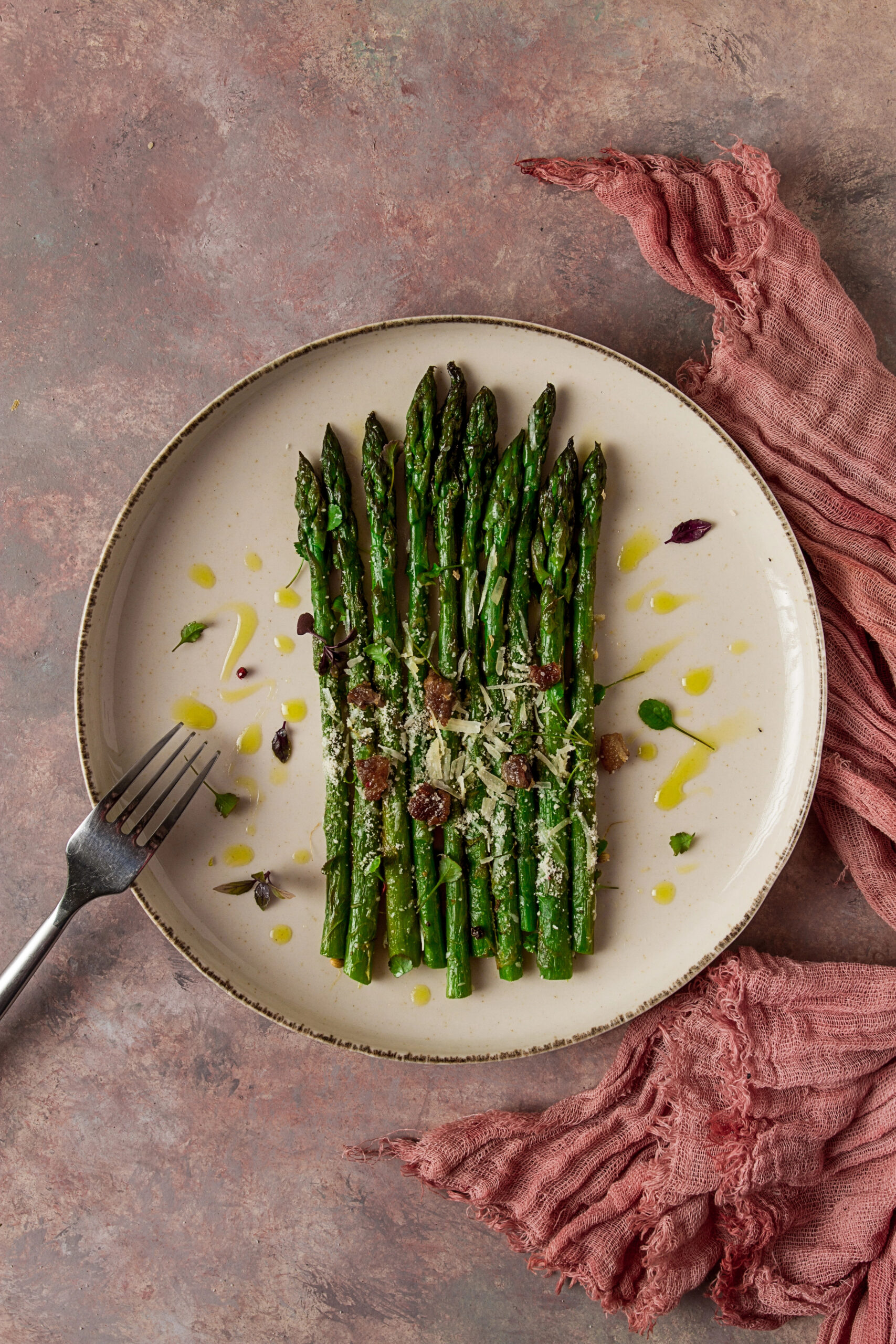 Grilled asparagus with parmesan and herbs on beige plate