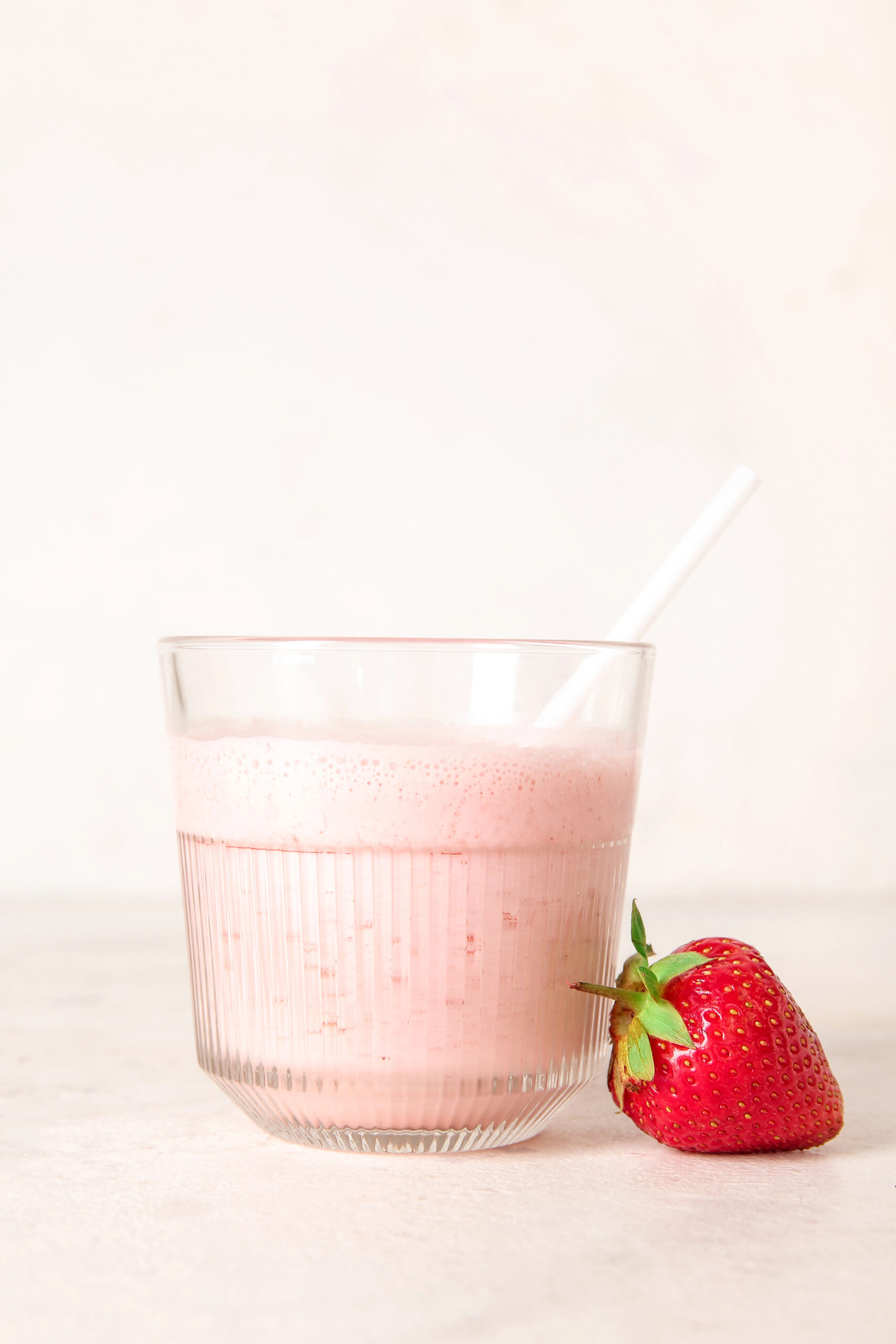 Glass of pink strawberry smoothie with straw