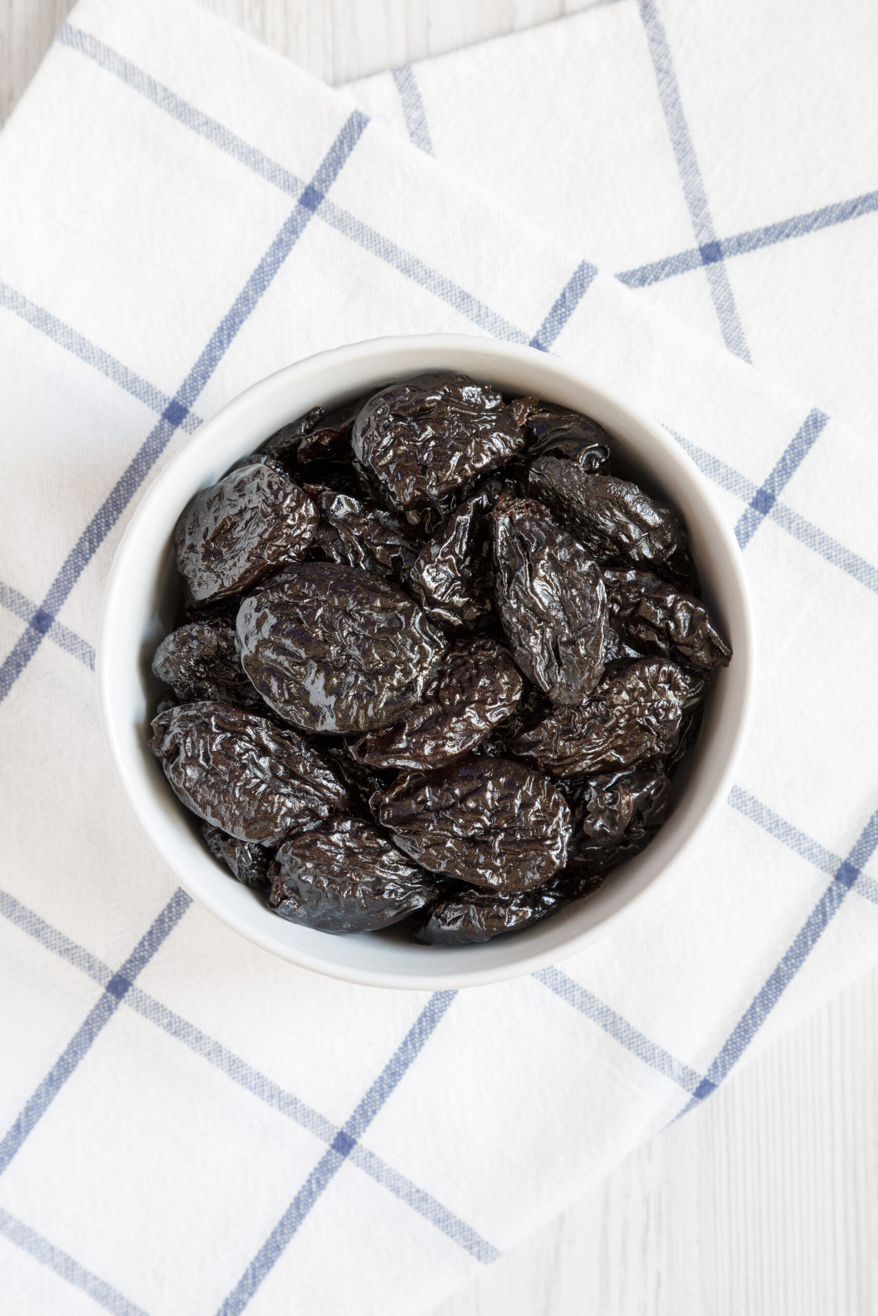 White bowl of dark dried prunes overhead view