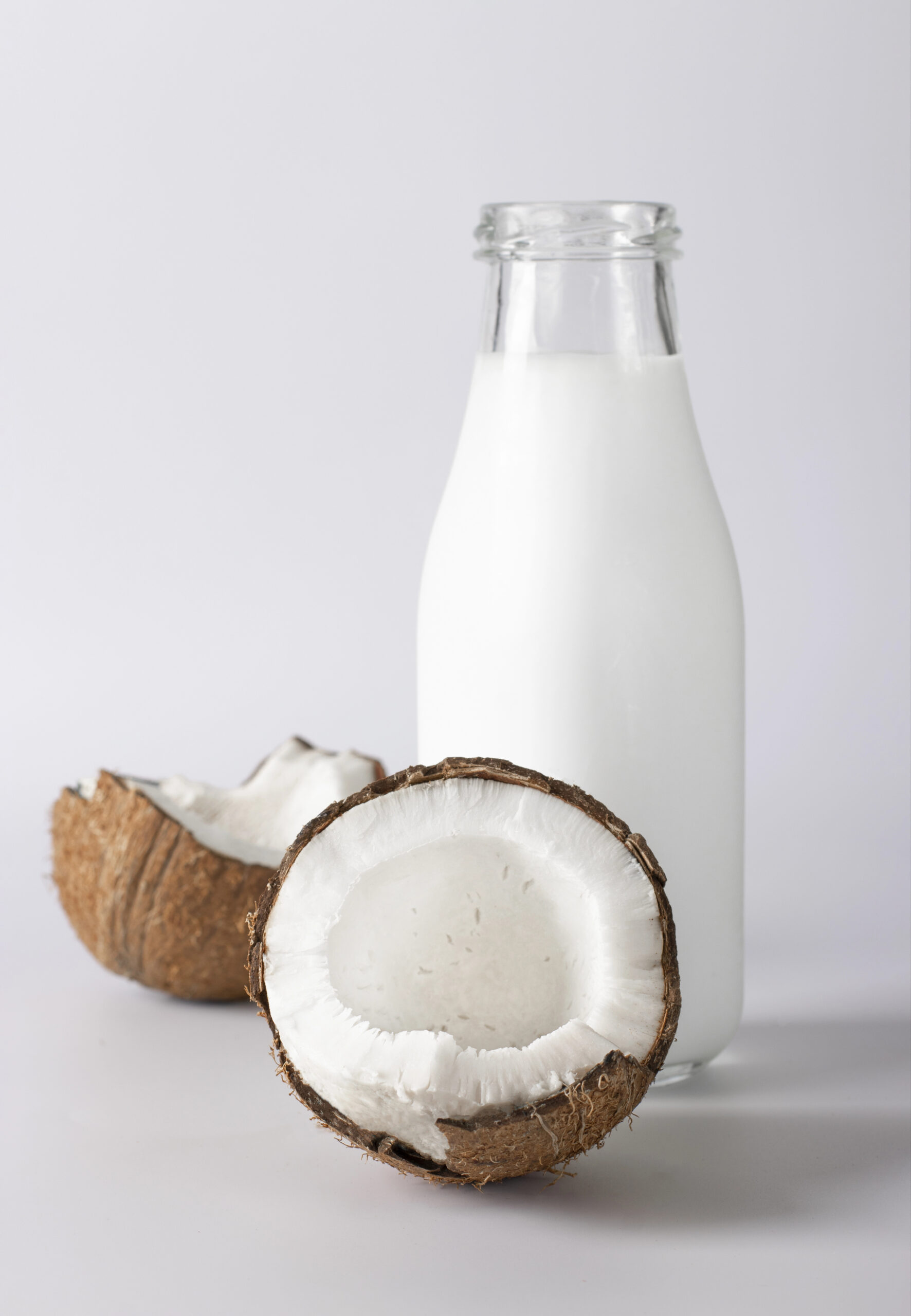 Coconut milk in glass bottle with halved fresh coconut