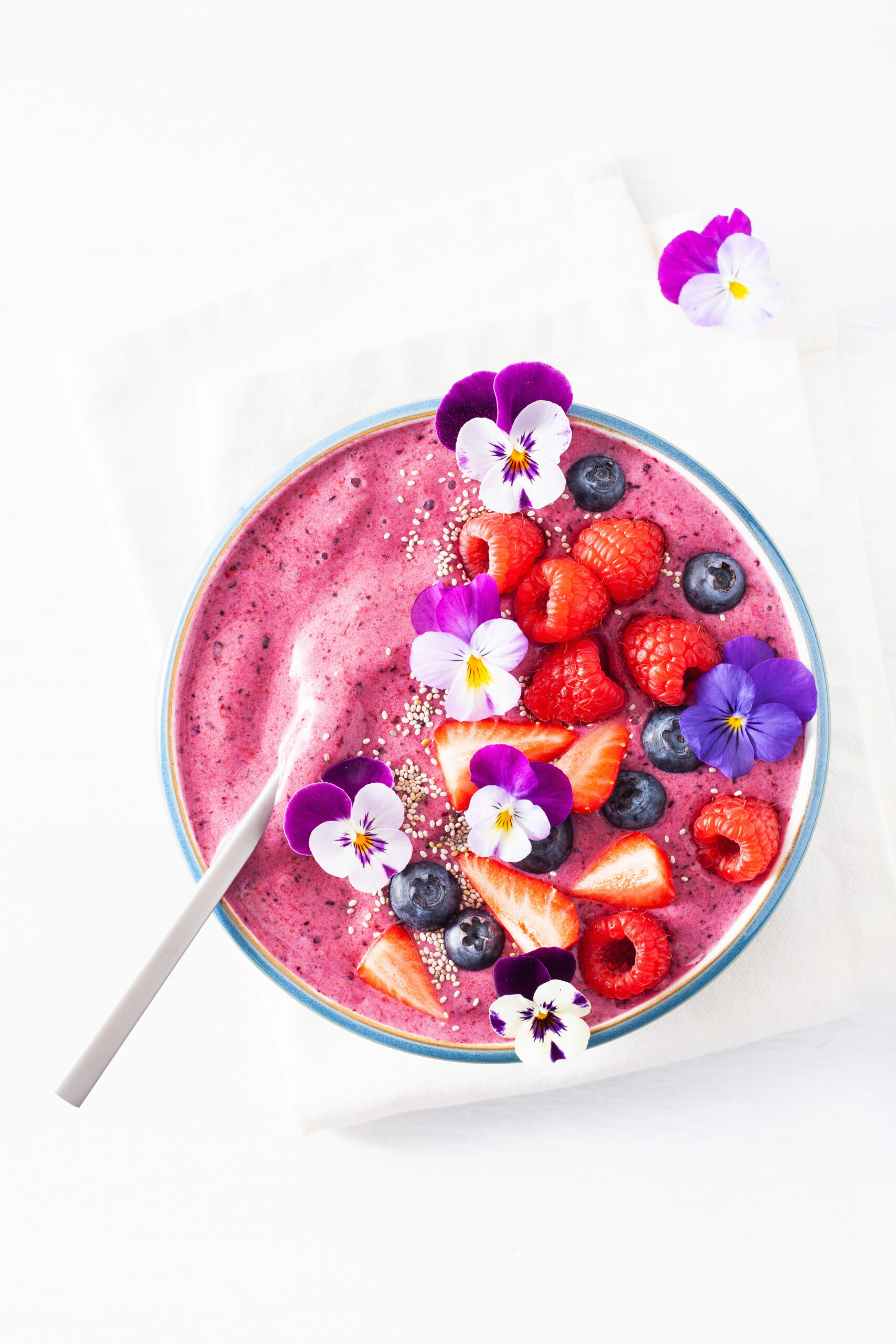 Pink smoothie bowl topped with berries and edible flowers
