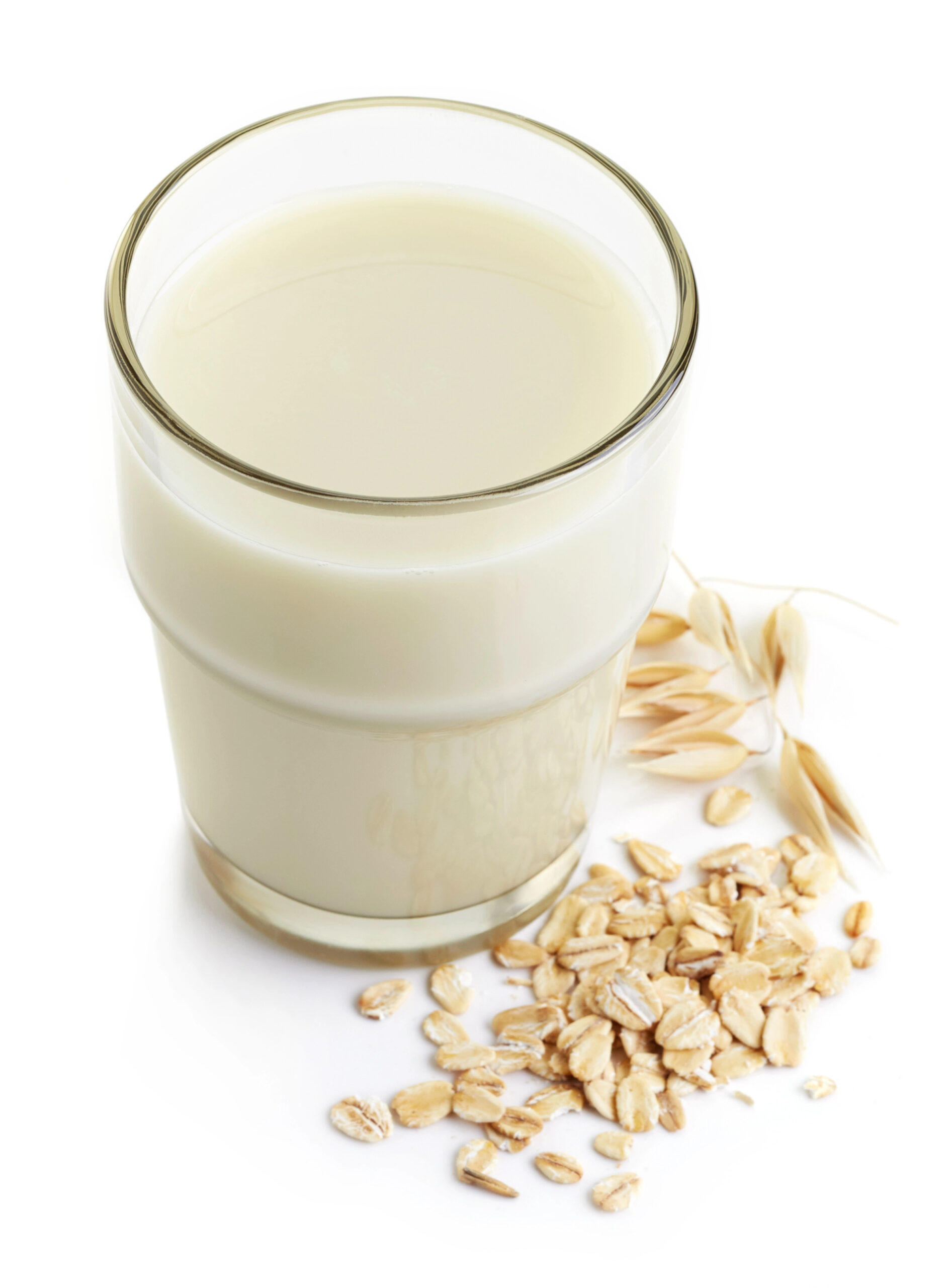 Glass of oat milk with oats scattered beside