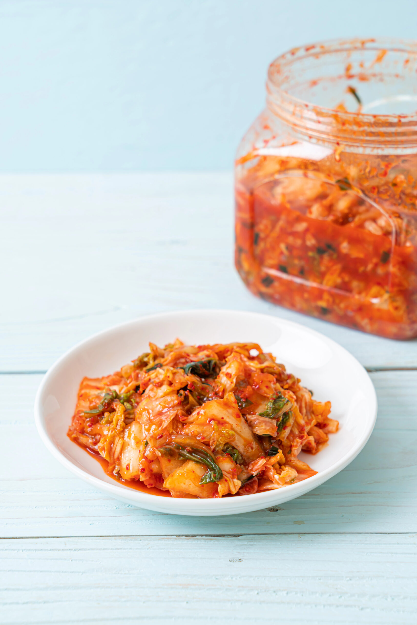 Kimchi served in white bowl with jar in background