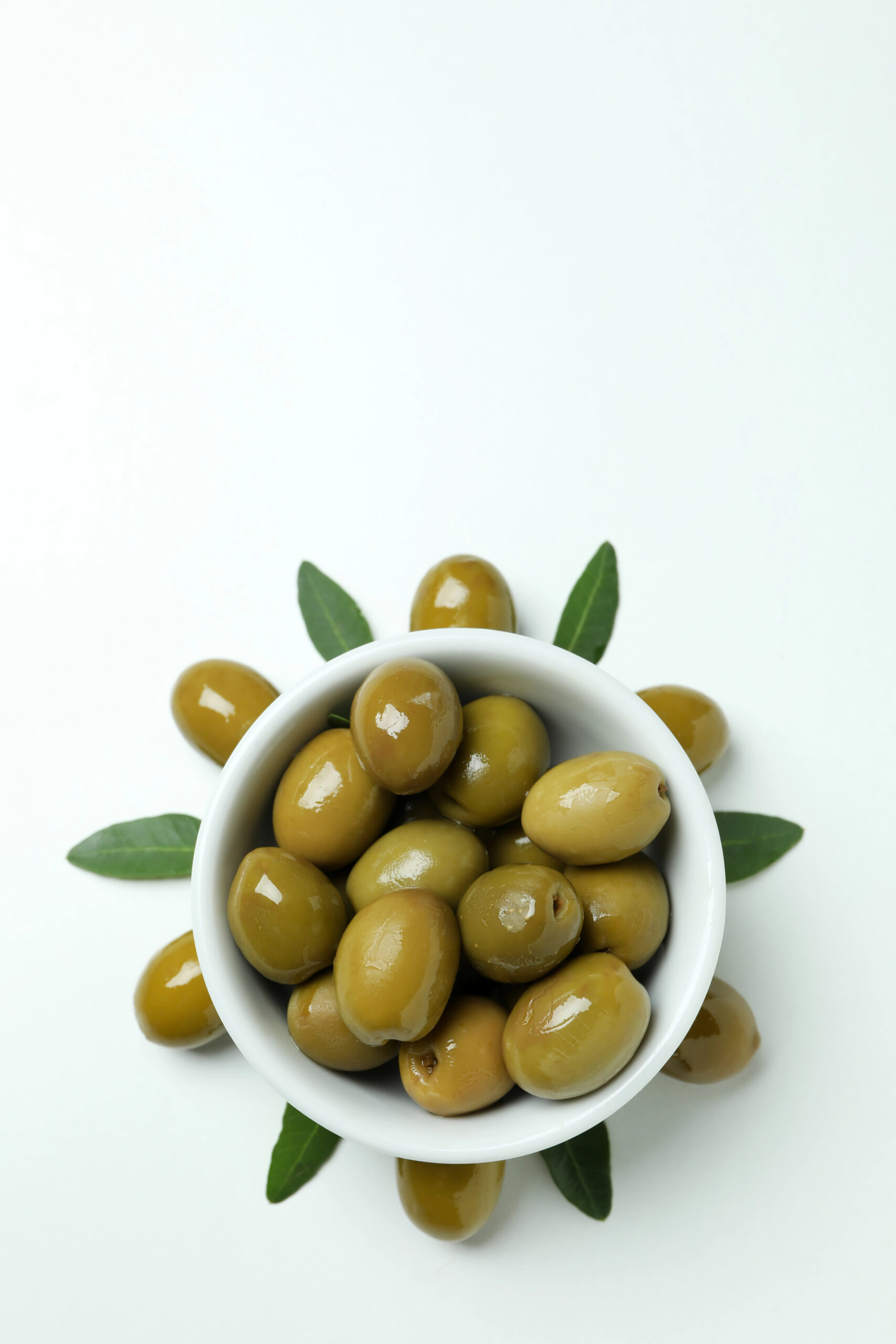 White bowl of green olives with leaves