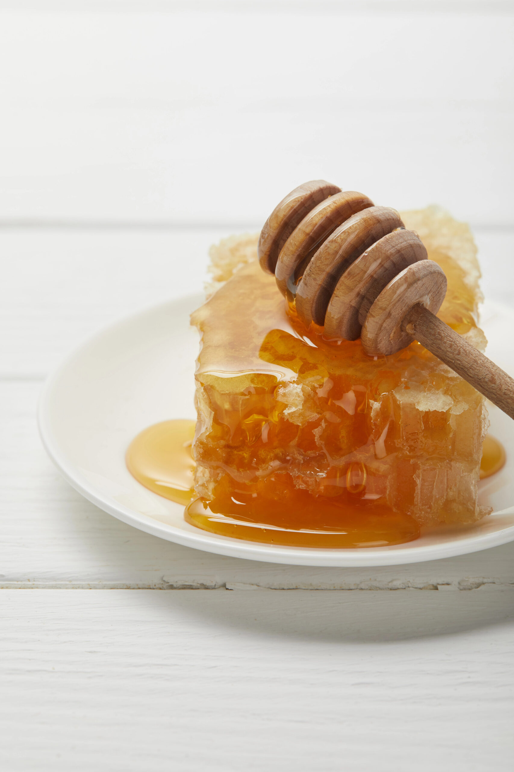 Honeycomb with honey dripping from wooden dipper