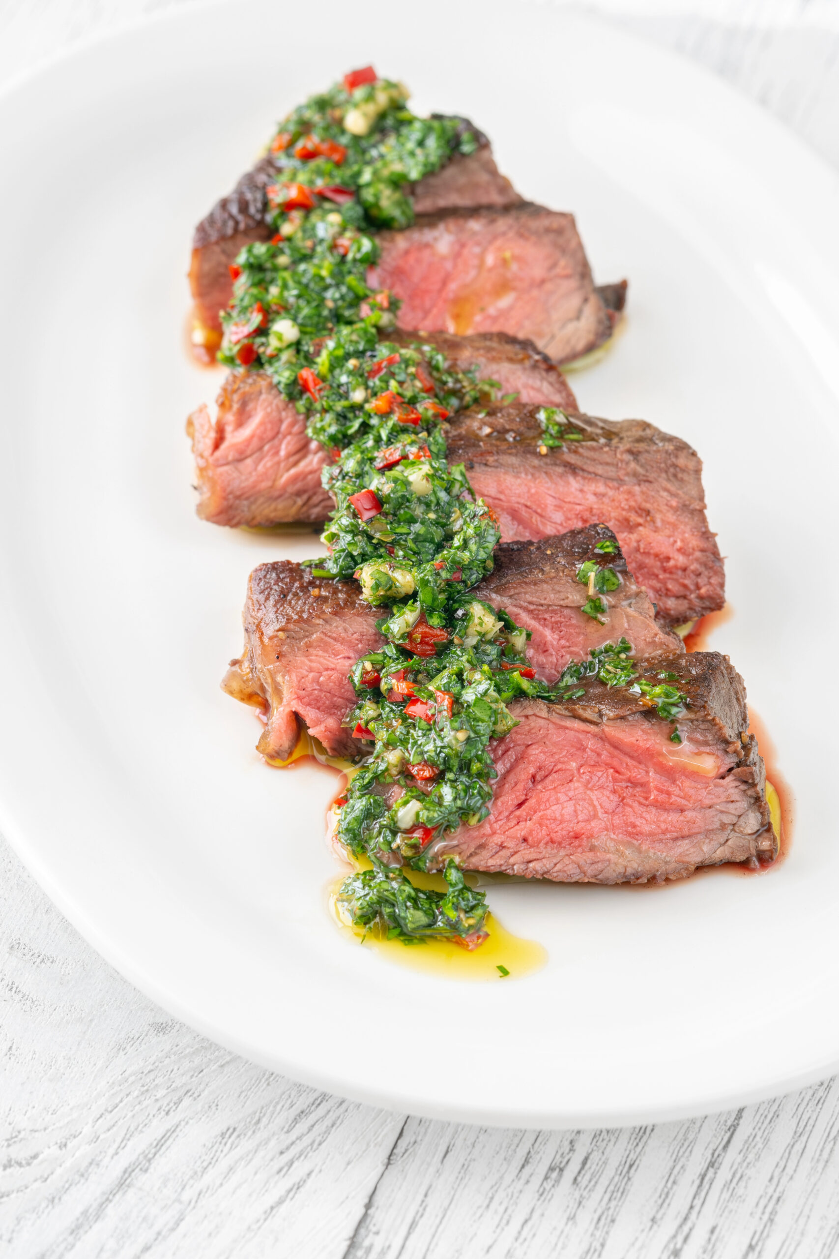 Sliced medium rare flank steak with green chimichurri