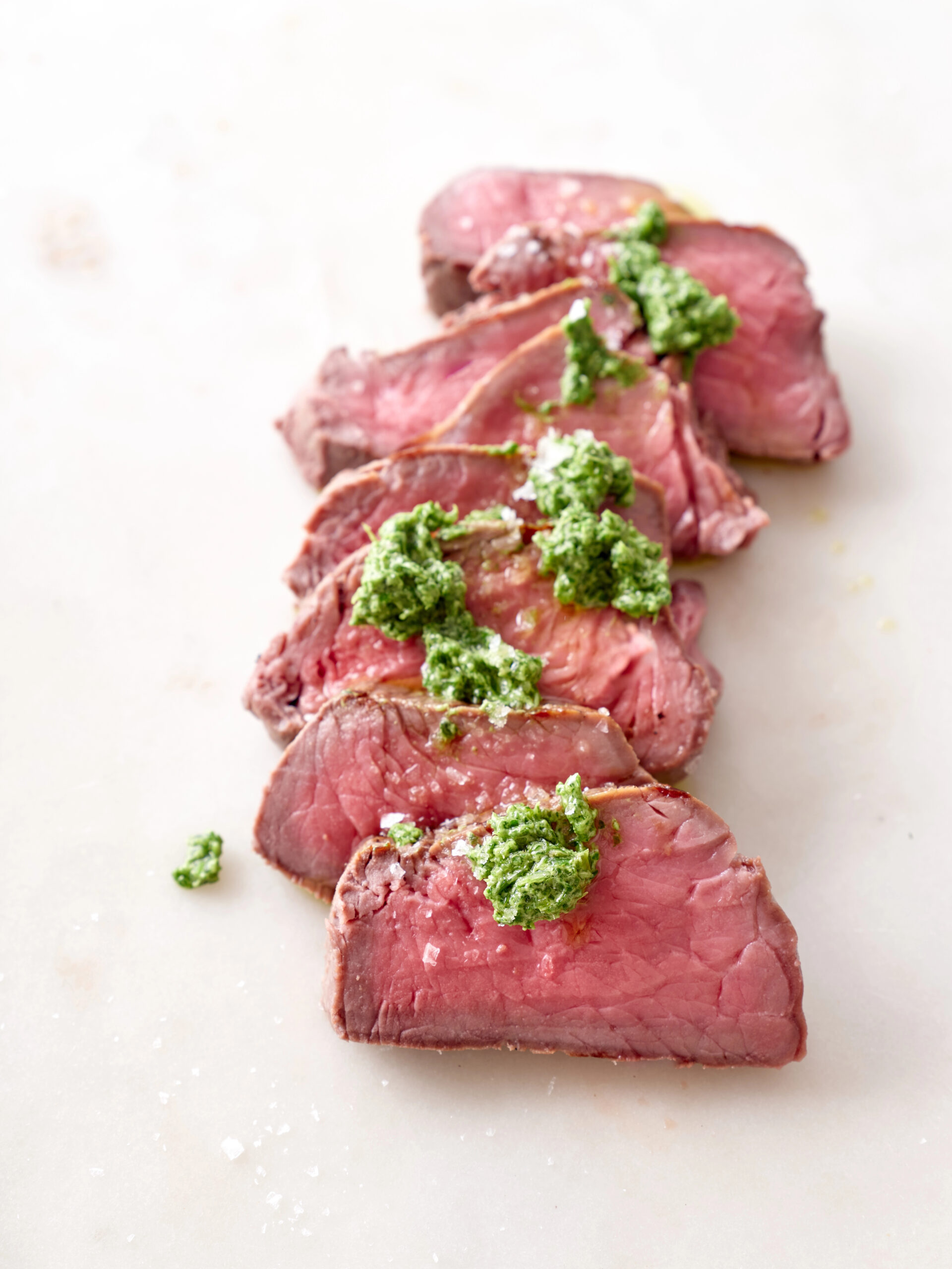 Fillet mignon arranged in a line with green herb sauce