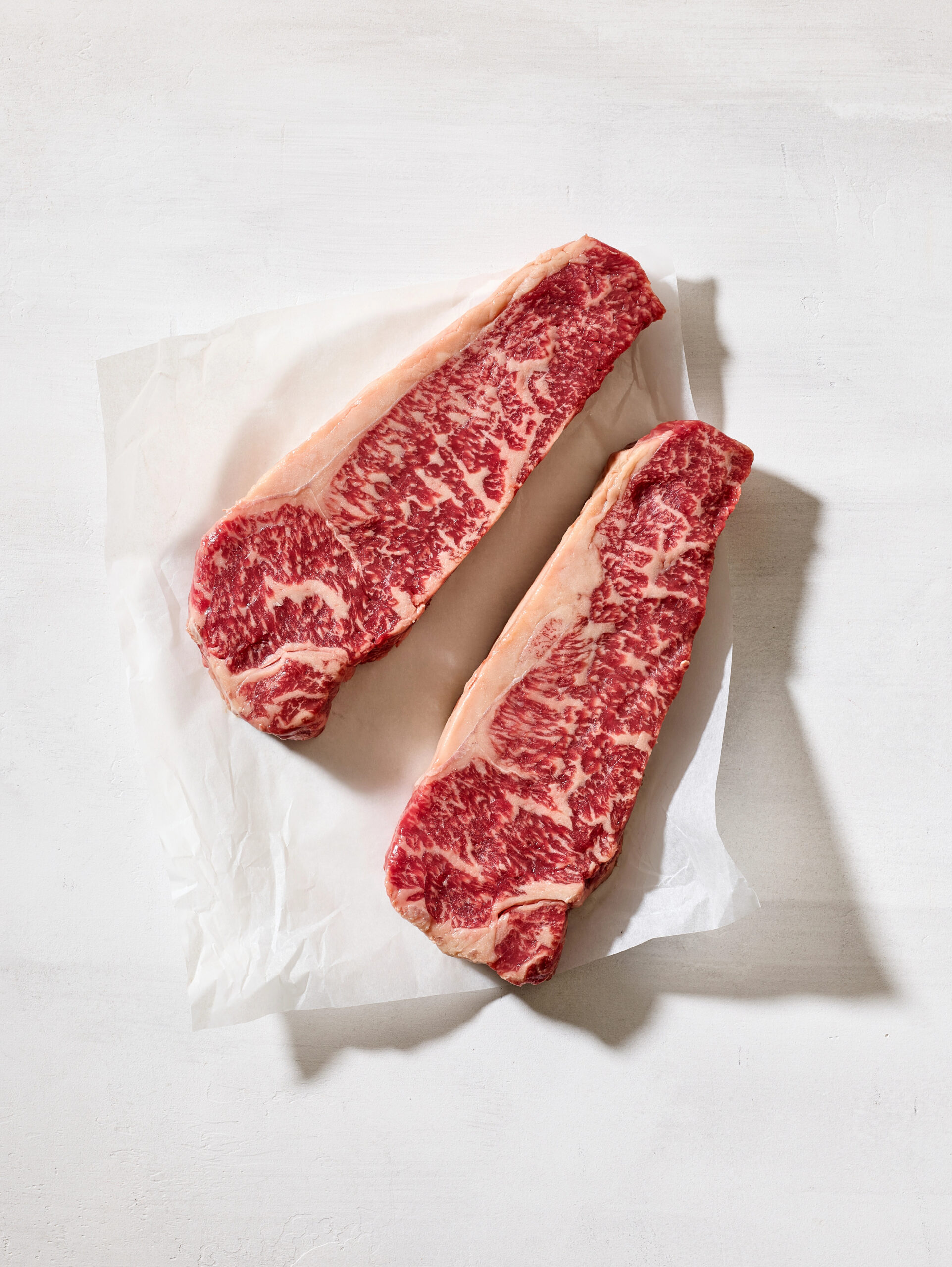 Two raw Wagyu steaks on white paper