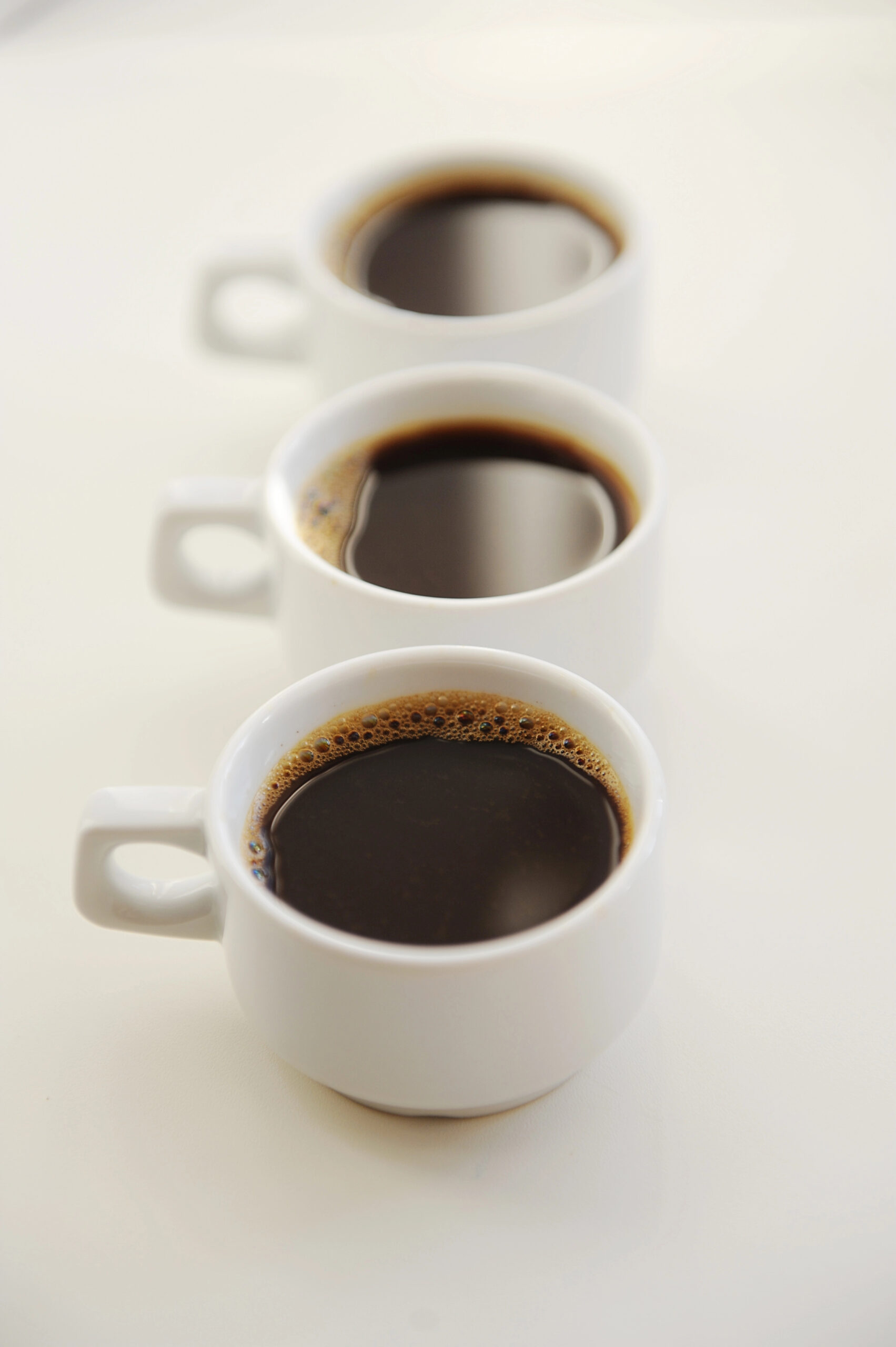 Three white cups filled with black coffee lined up vertically