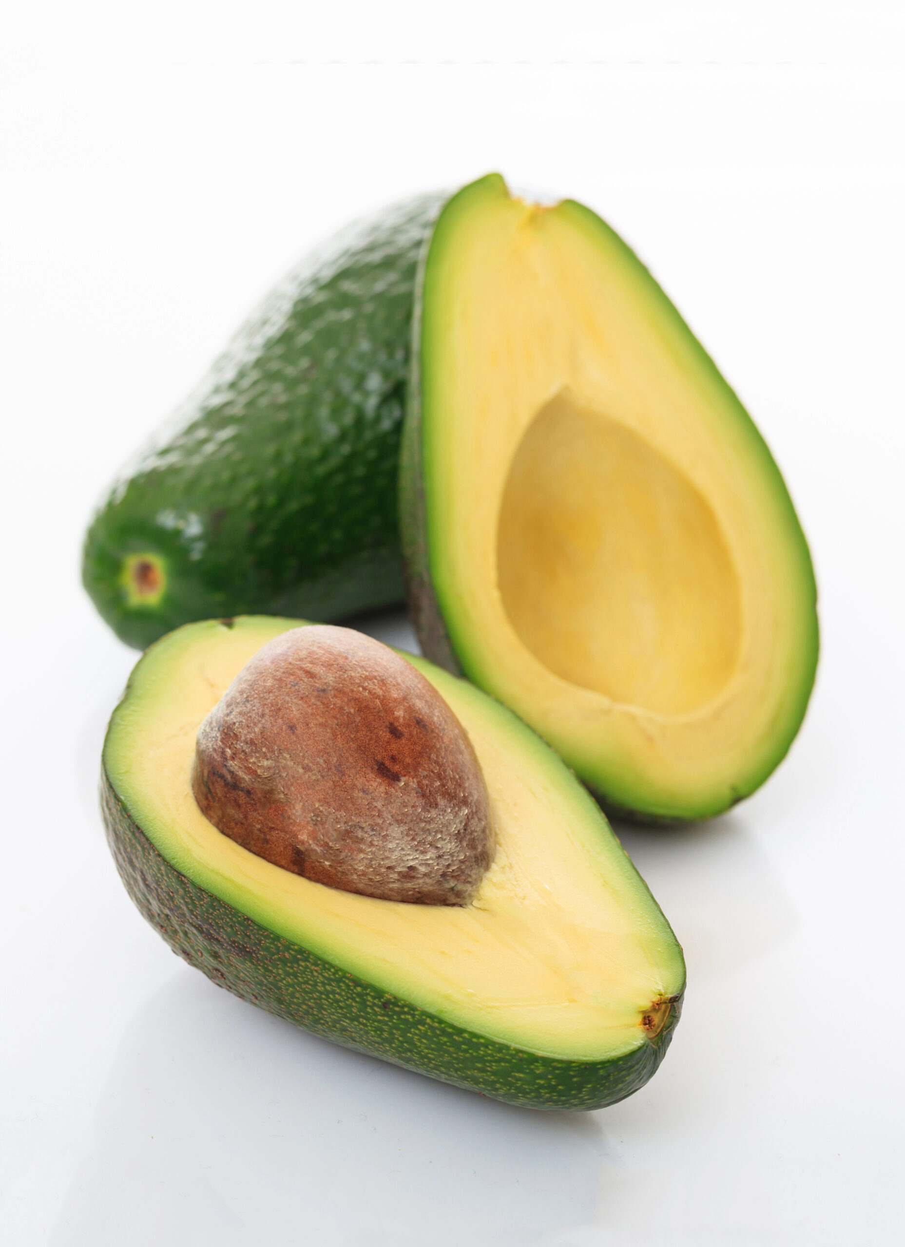 Whole avocado and two halved avocados showing pits